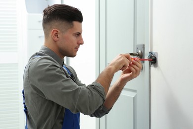 Professional electrician with screwdriver repairing light switch indoors