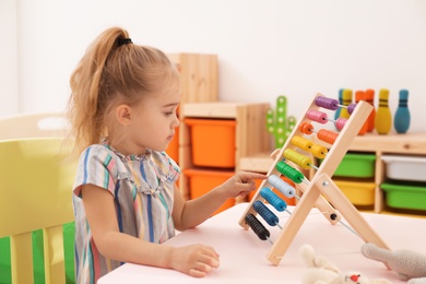 Cute child playing with wooden abacus at table in room