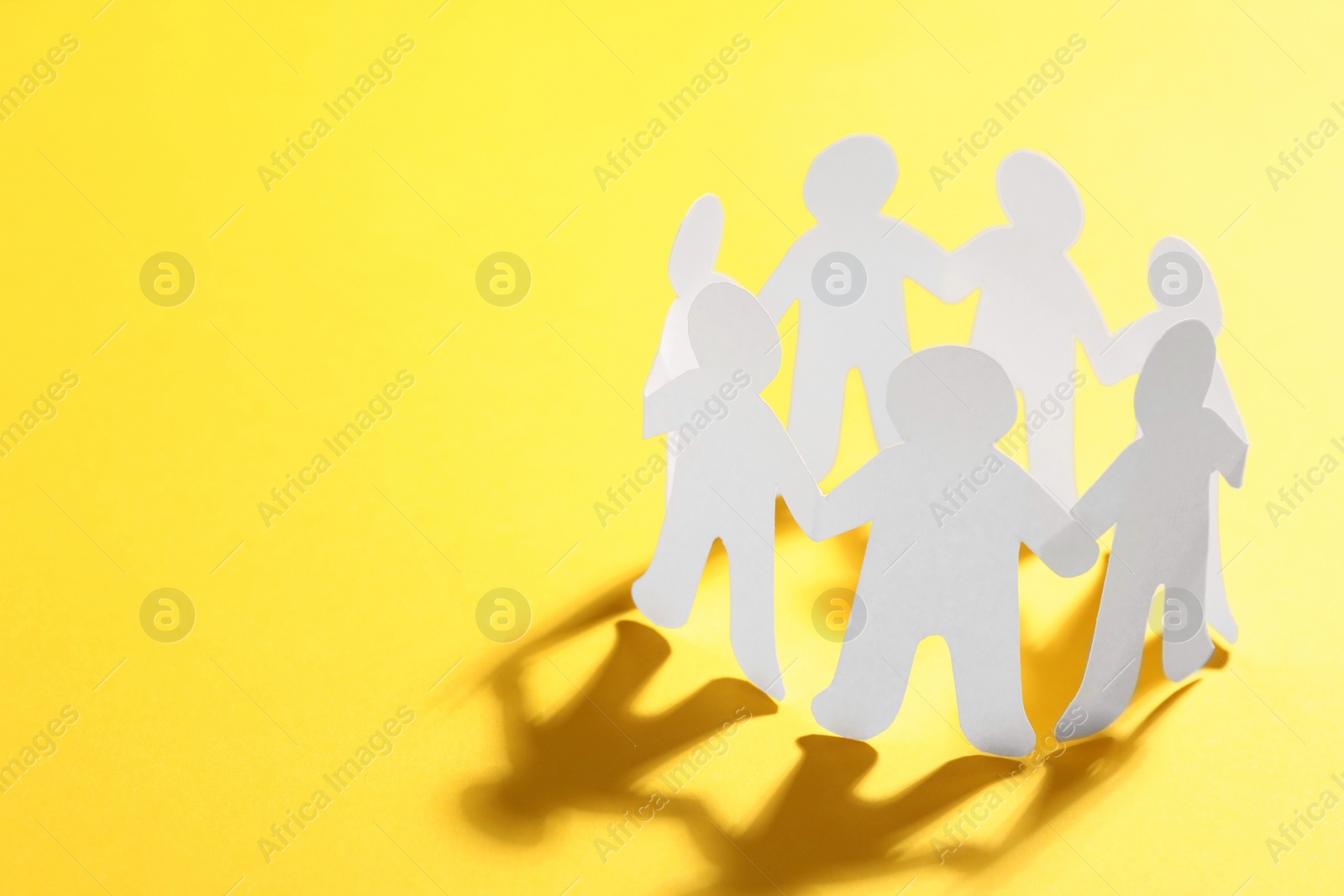 Photo of Paper people chain making circle on yellow background, space for text. Unity concept