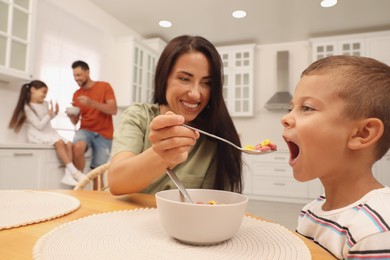 Photo of Happy mother feeding her son at table in kitchen