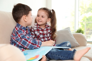 Photo of Cute children reading book on sofa in living room