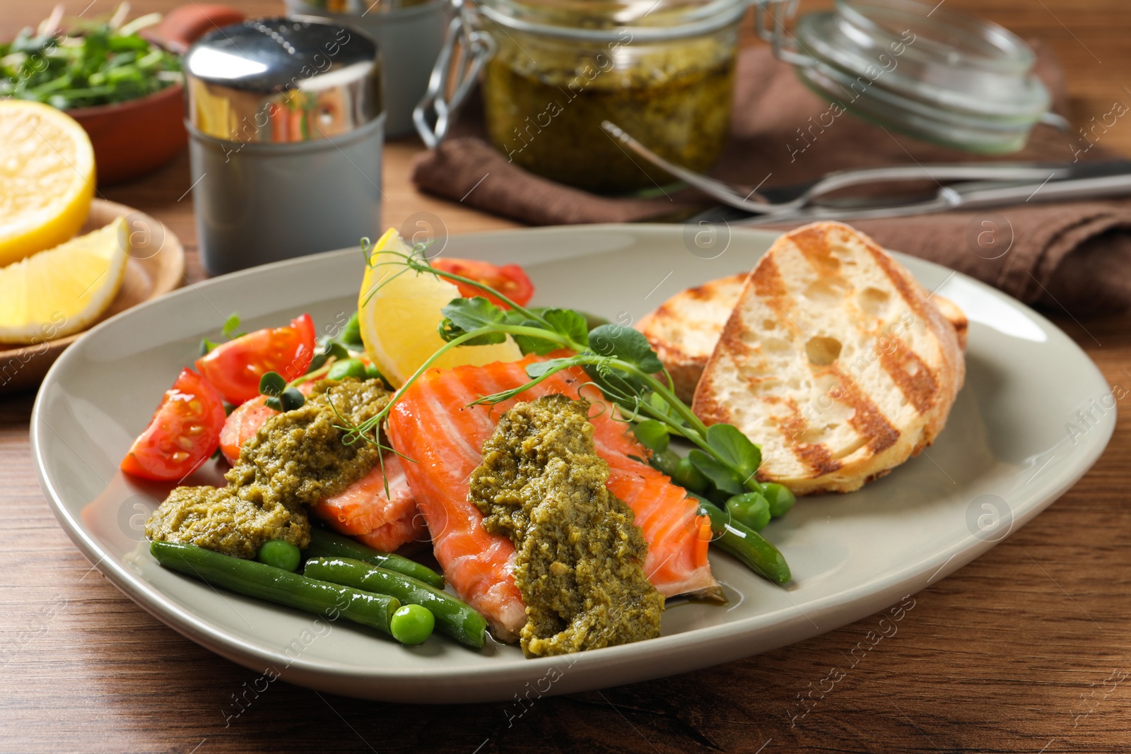 Photo of Tasty cooked salmon with pesto sauce served on wooden table, closeup