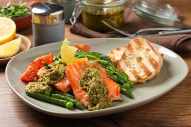 Photo of Tasty cooked salmon with pesto sauce served on wooden table, closeup