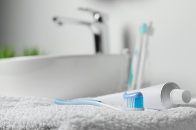 Photo of Plastic toothbrush with paste and tube on white towel in bathroom, closeup. Space for text