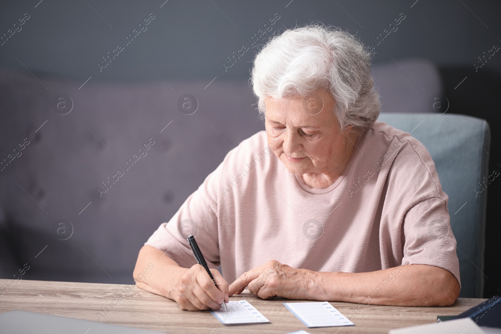 Photo of Portrait of senior woman filling out lottery ticket at table