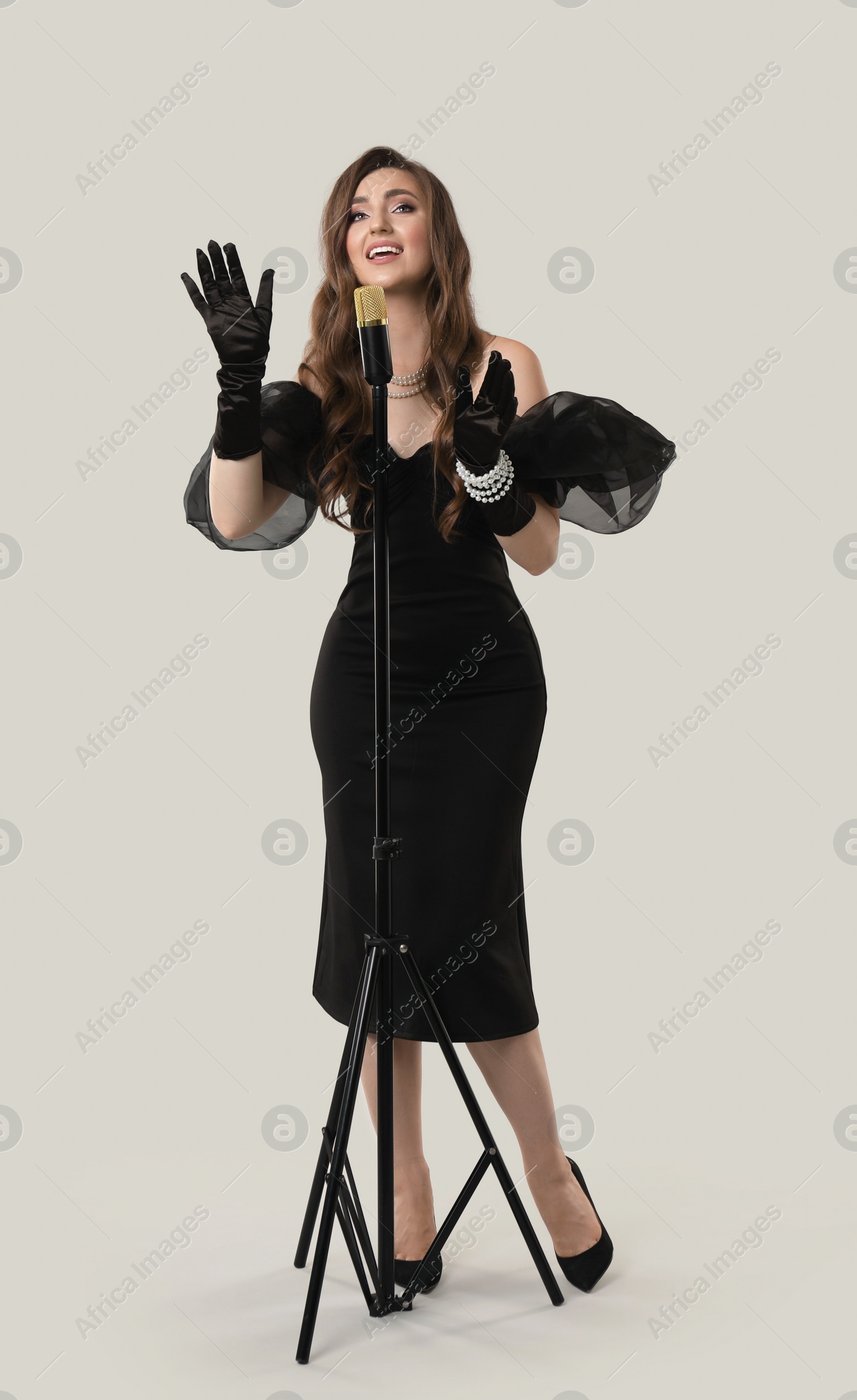 Photo of Beautiful young woman in stylish dress with microphone singing on light grey background