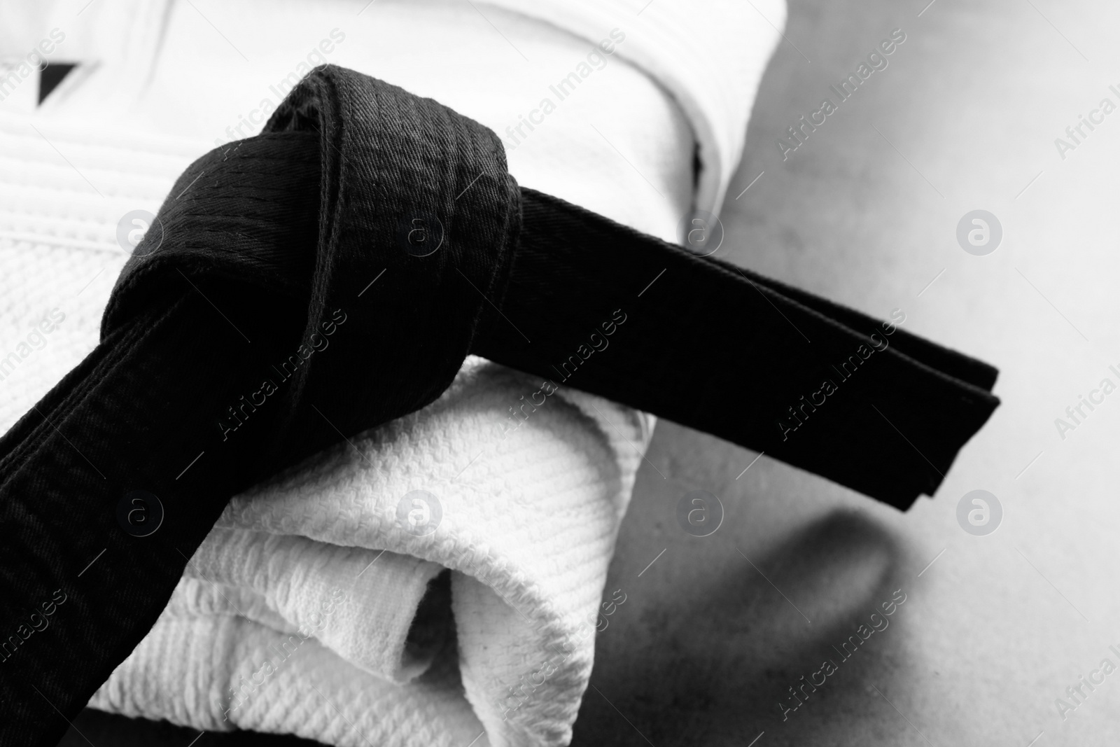 Photo of Folded white kimono and black belt on grey stone background, closeup