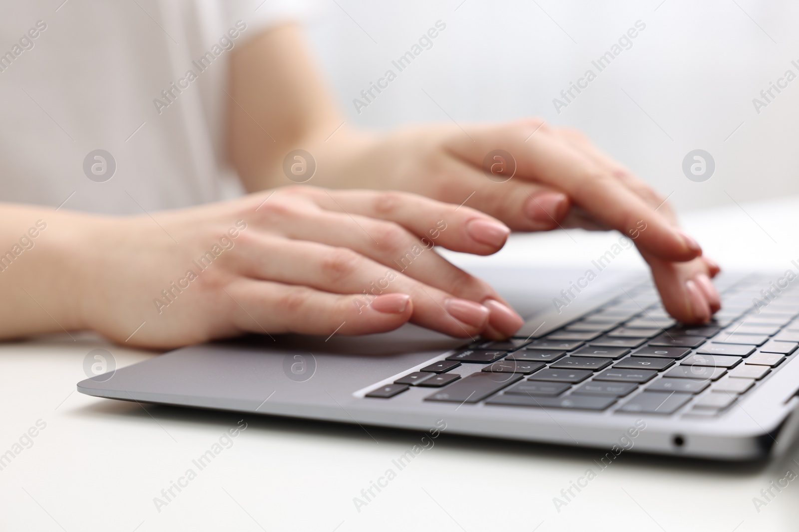 Photo of E-learning. Woman using laptop at white table indoors, closeup