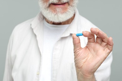 Photo of Senior man with pill on grey background, closeup