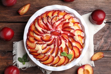 Photo of Delicious cake with plums on wooden table, flat lay