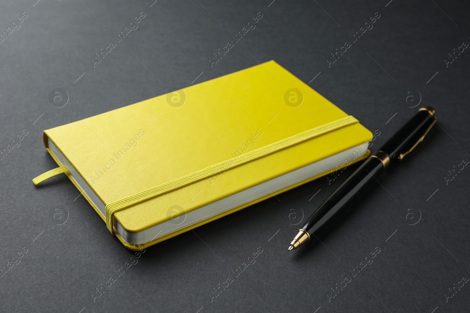 Photo of Closed yellow notebook and pen on black background