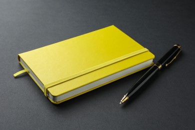 Photo of Closed yellow notebook and pen on black background