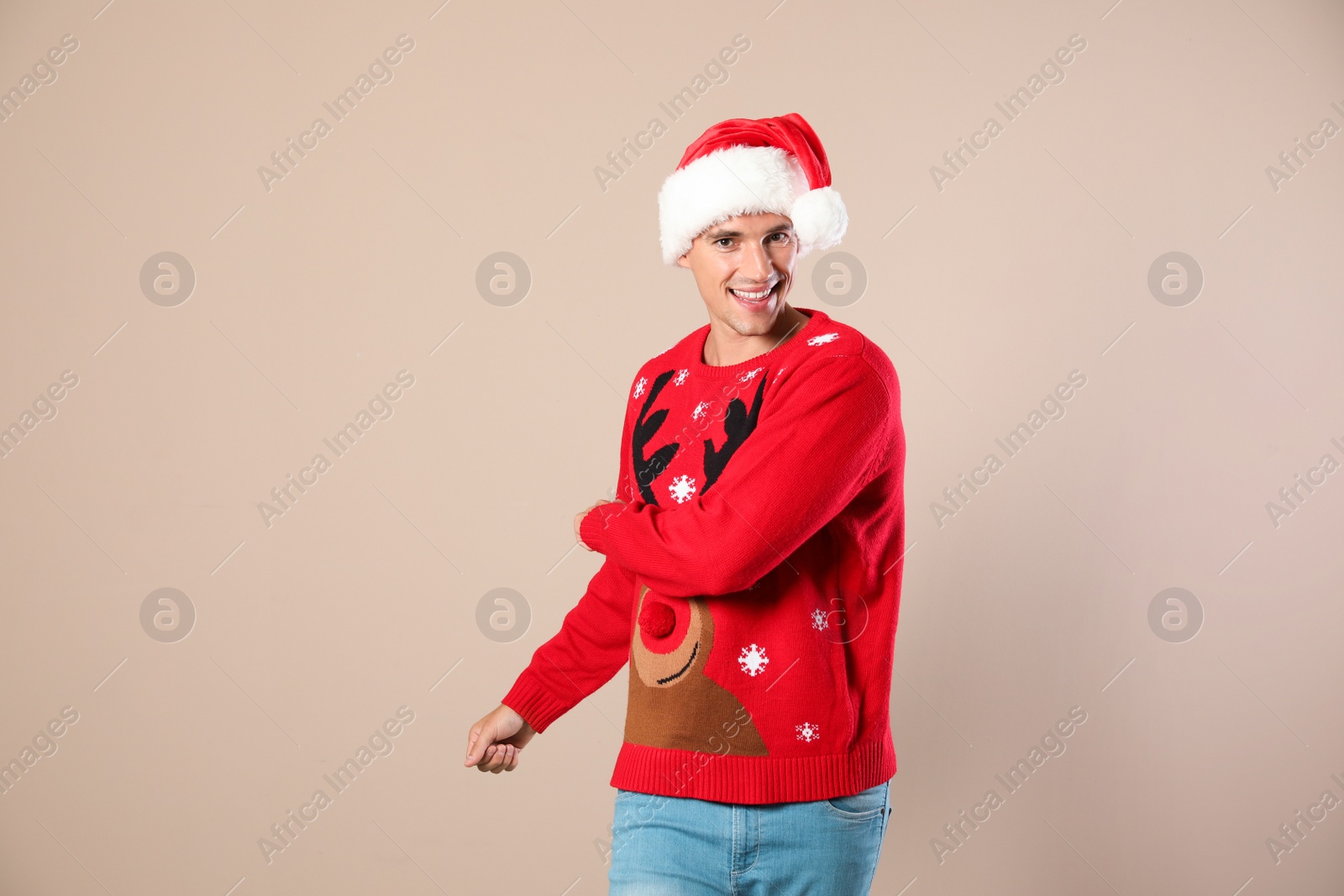 Photo of Portrait of young man in Christmas sweater and Santa hat on beige background