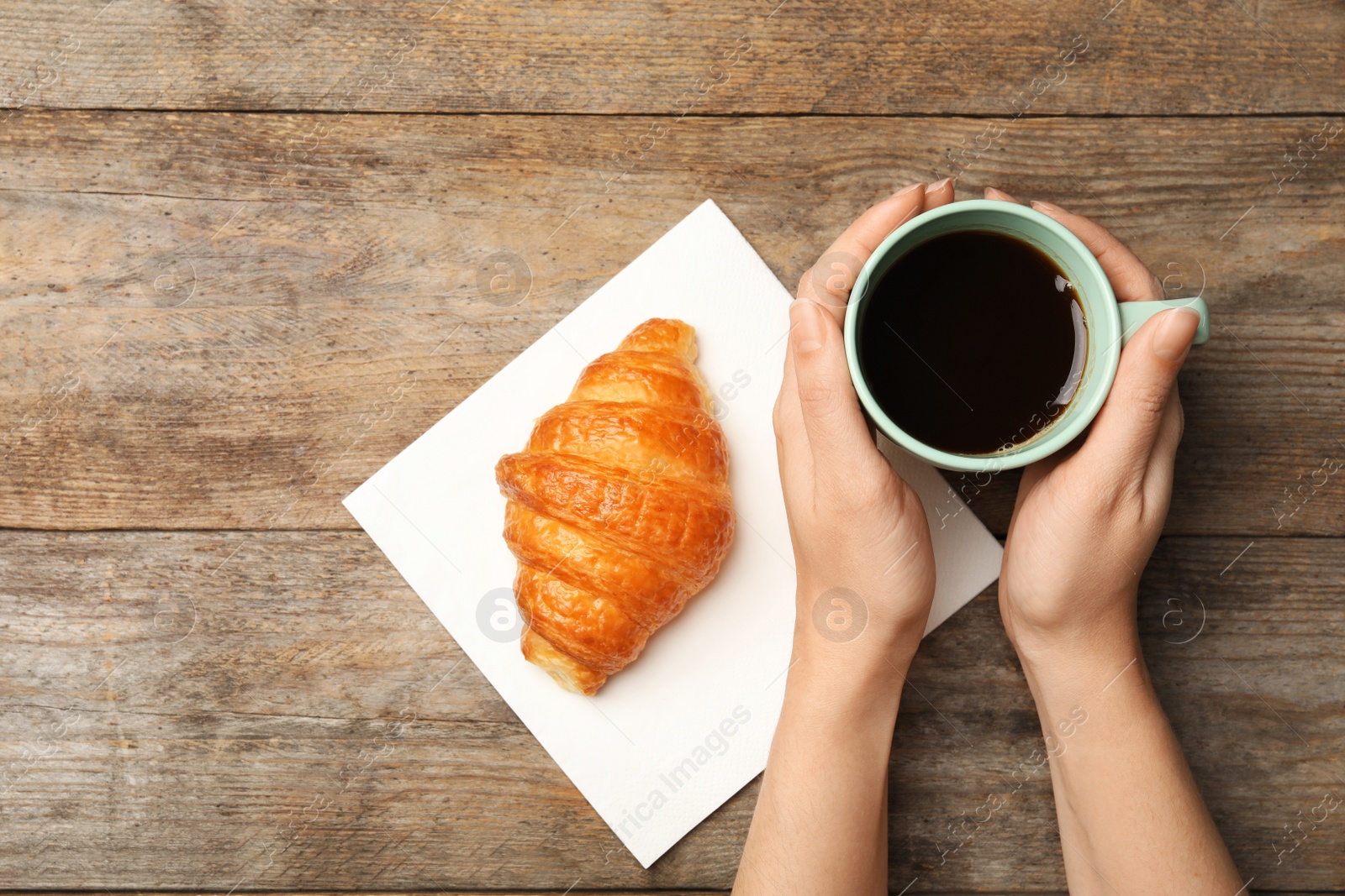 Photo of Woman with cup of coffee and tasty croissant at wooden table, flat lay. Space for text
