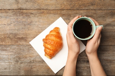 Woman with cup of coffee and tasty croissant at wooden table, flat lay. Space for text