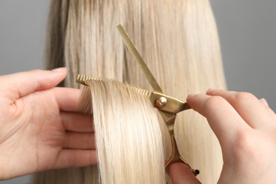 Hairdresser cutting client's hair with scissors on light grey background, closeup