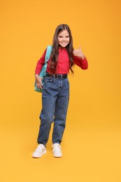 Cute schoolgirl showing thumbs up on orange background