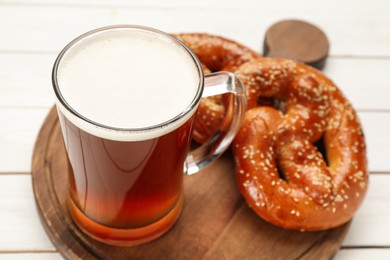 Mug of beer with tasty freshly baked pretzels on white table, closeup
