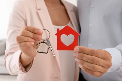Photo of Young couple holding key and house model, closeup. Real estate agent services