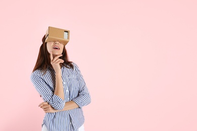 Young woman using cardboard virtual reality headset on color background. Space for text