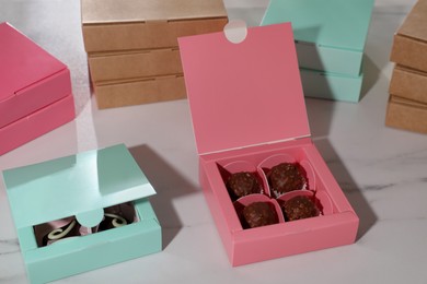 Photo of Boxes with delicious candies on white marble table, closeup. Production line