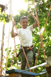 Little African-American boy climbing in adventure park. Summer camp