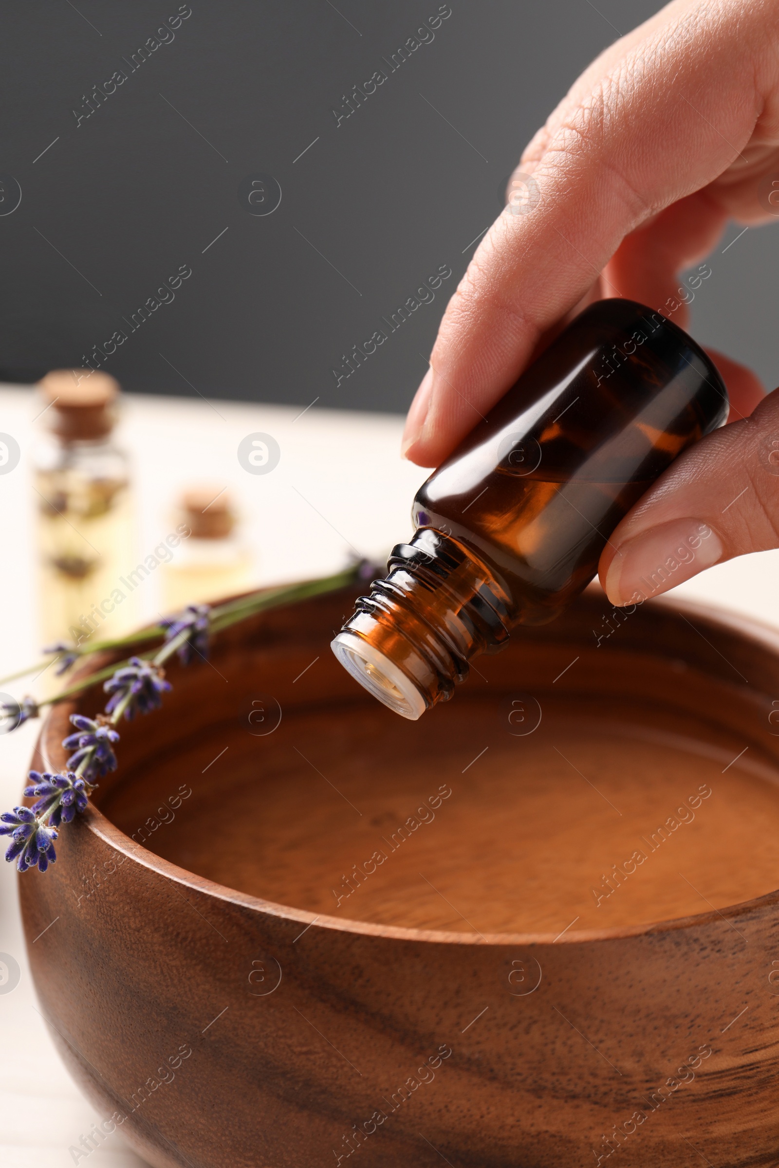 Photo of Woman dripping lavender essential oil from bottle into bowl, closeup