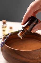 Woman dripping lavender essential oil from bottle into bowl, closeup