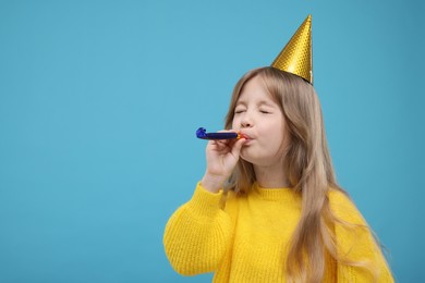 Photo of Cute little girl in party hat with blower on light blue background. Space for text
