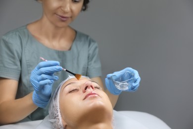 Photo of Cosmetologist applying chemical peel product on client's face in salon