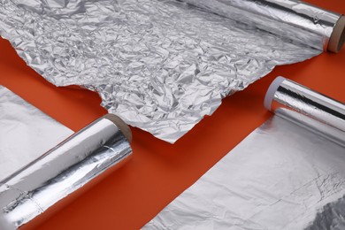 Photo of Different rolls of aluminum foil on orange background, closeup