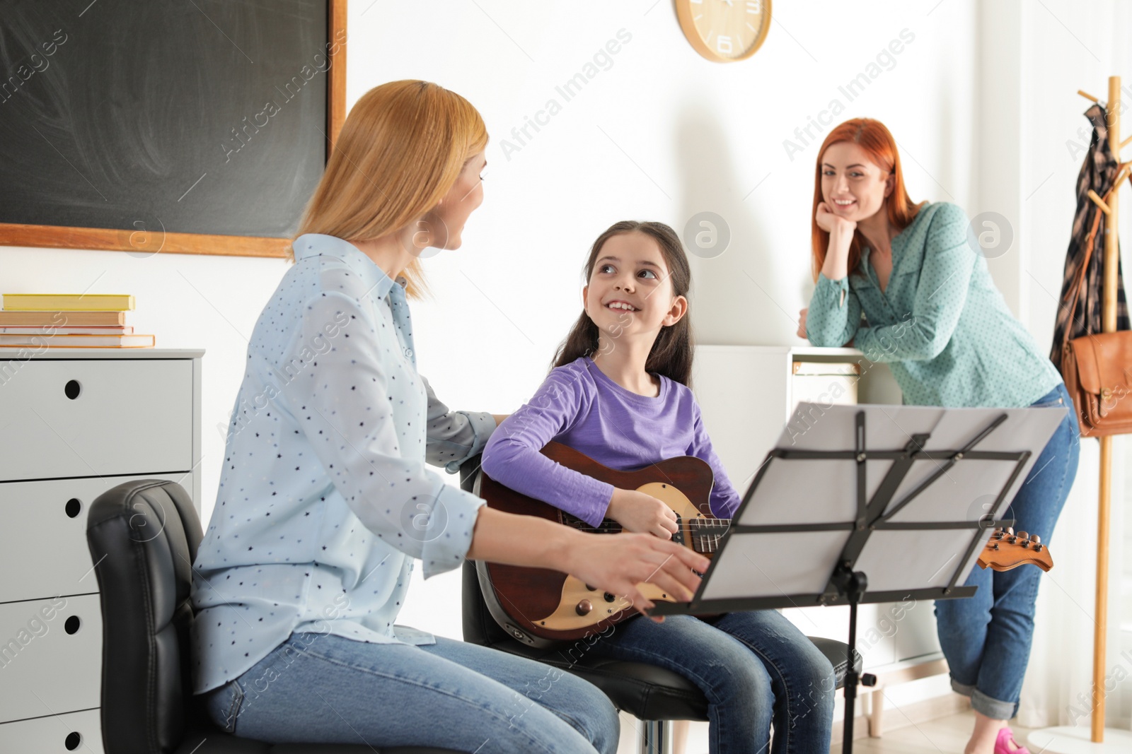 Photo of Little girl with her teacher and mother at music lesson. Learning notes
