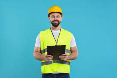 Photo of Engineer in hard hat holding clipboard on light blue background