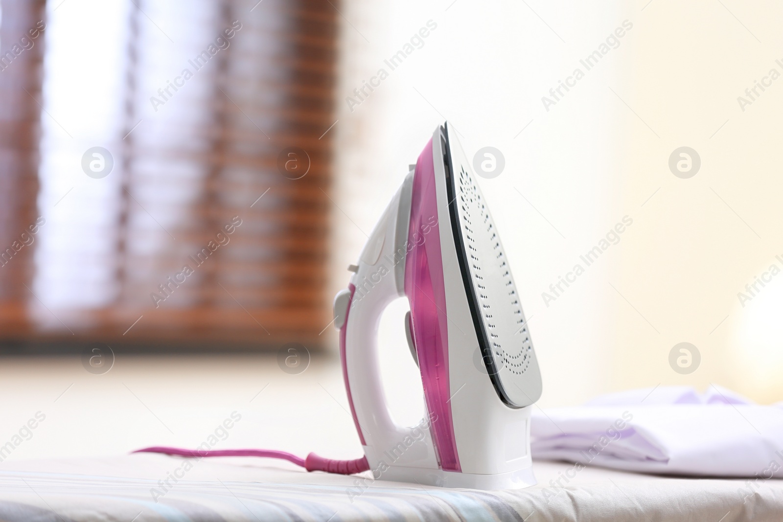 Photo of Modern iron and shirt on board in room