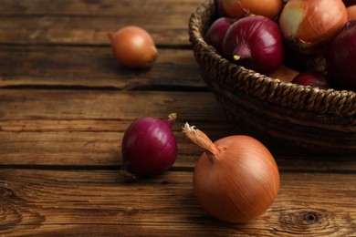 Photo of Onion bulbs and basket on wooden table