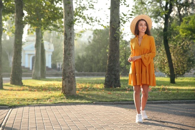 Photo of Beautiful young woman wearing stylish yellow dress and straw hat in park