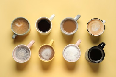 Many different cups with aromatic coffee on yellow table, flat lay