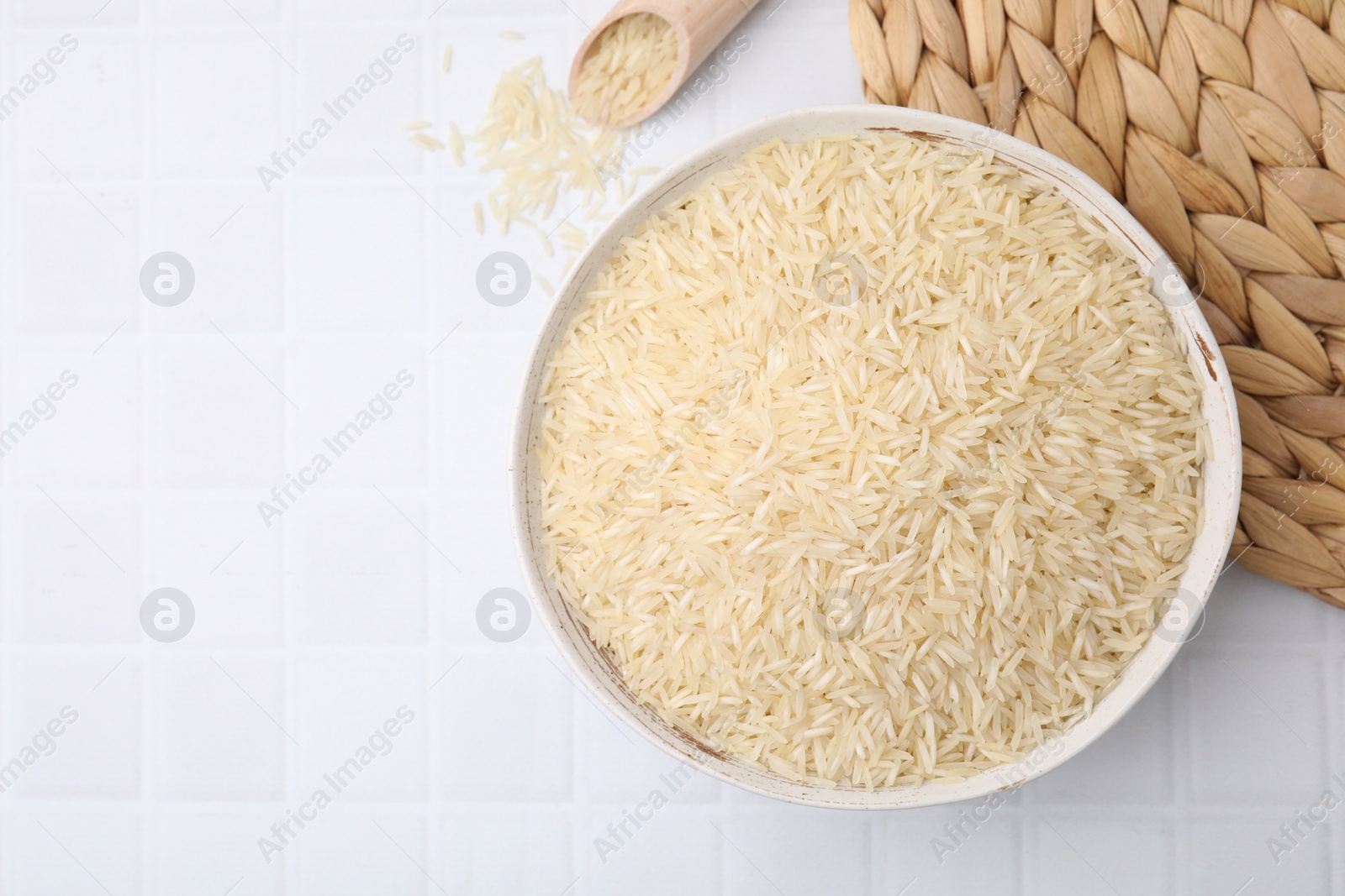 Photo of Bowl and scoop with raw rice on white tiled table, flat lay. Space for text