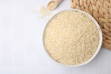 Photo of Bowl and scoop with raw rice on white tiled table, flat lay. Space for text