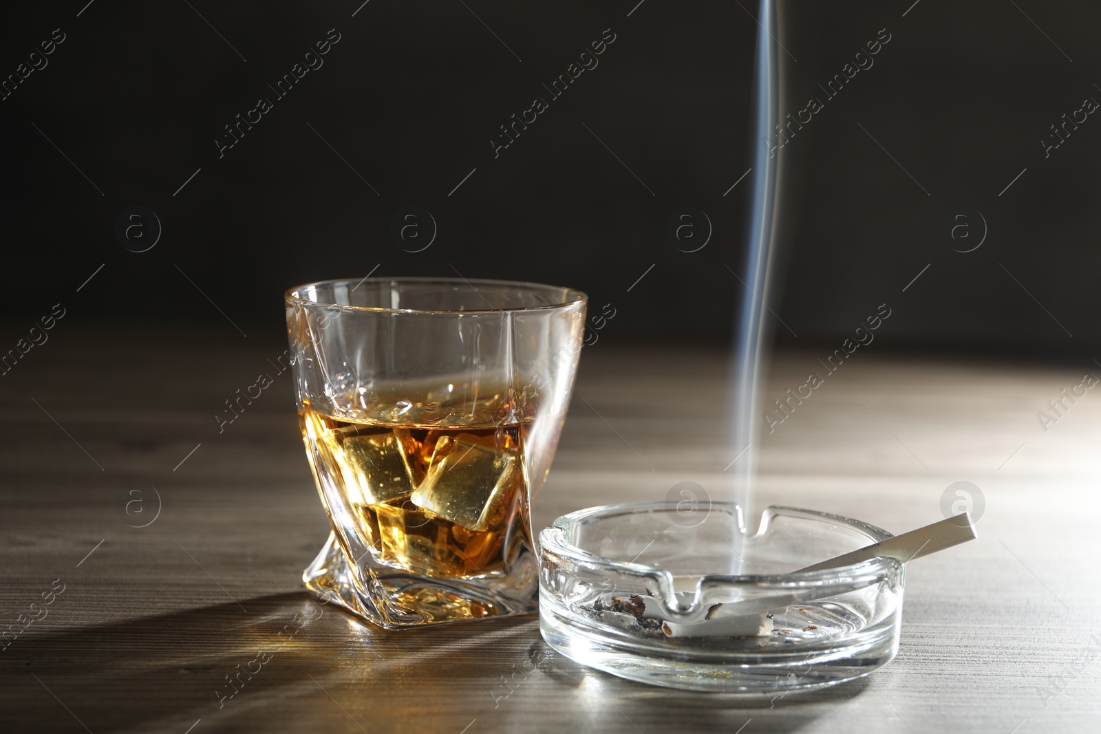 Photo of Alcohol addiction. Whiskey in glass, cigarettes and ashtray on wooden table