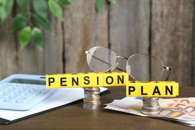 Photo of Yellow cubes with phrase Pension Plan, money, glasses and calculator on wooden table. Retirement concept