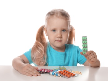 Photo of Little child with many different pills on white background. Danger of medicament intoxication