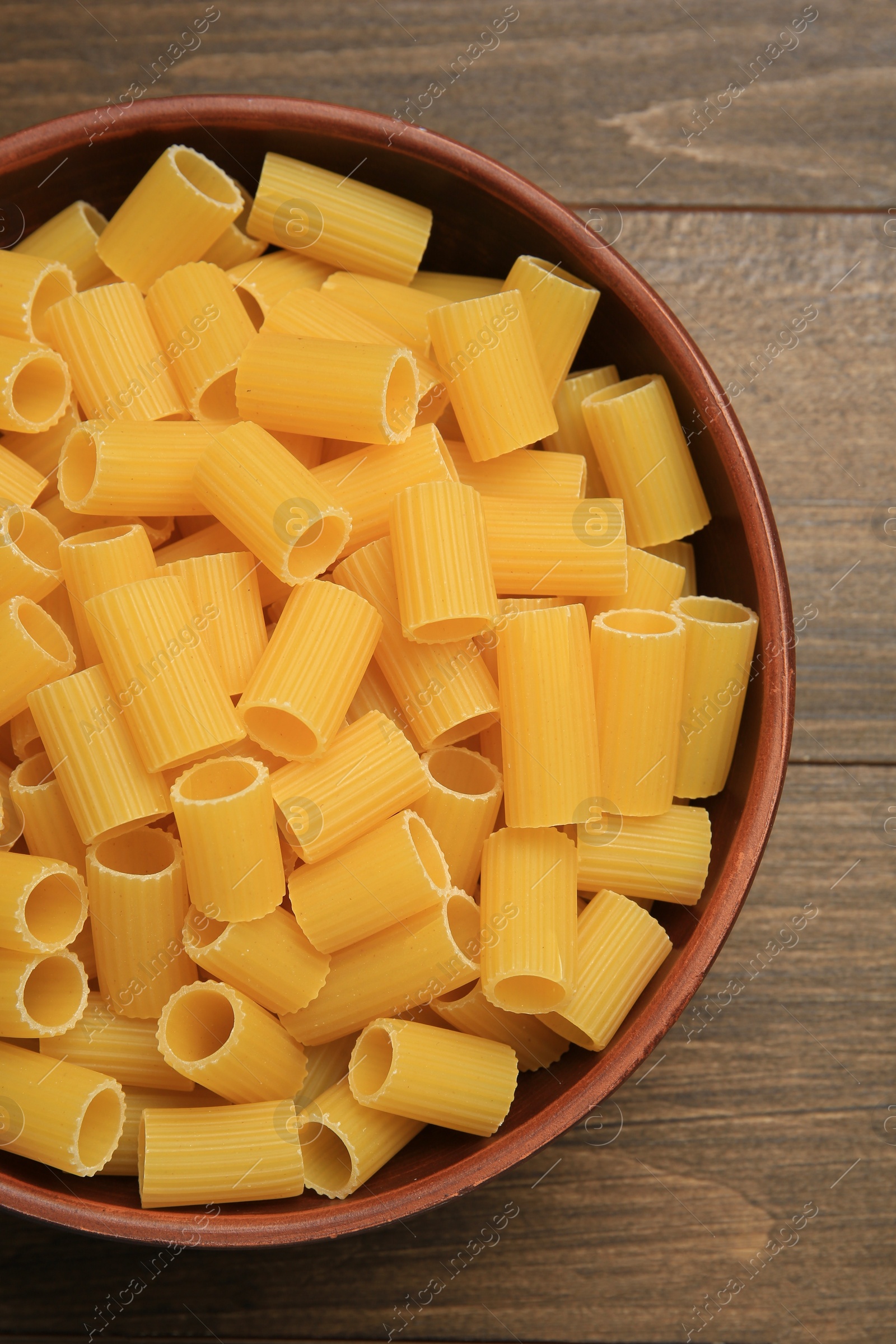 Photo of Raw rigatoni pasta in bowl on wooden table, top view