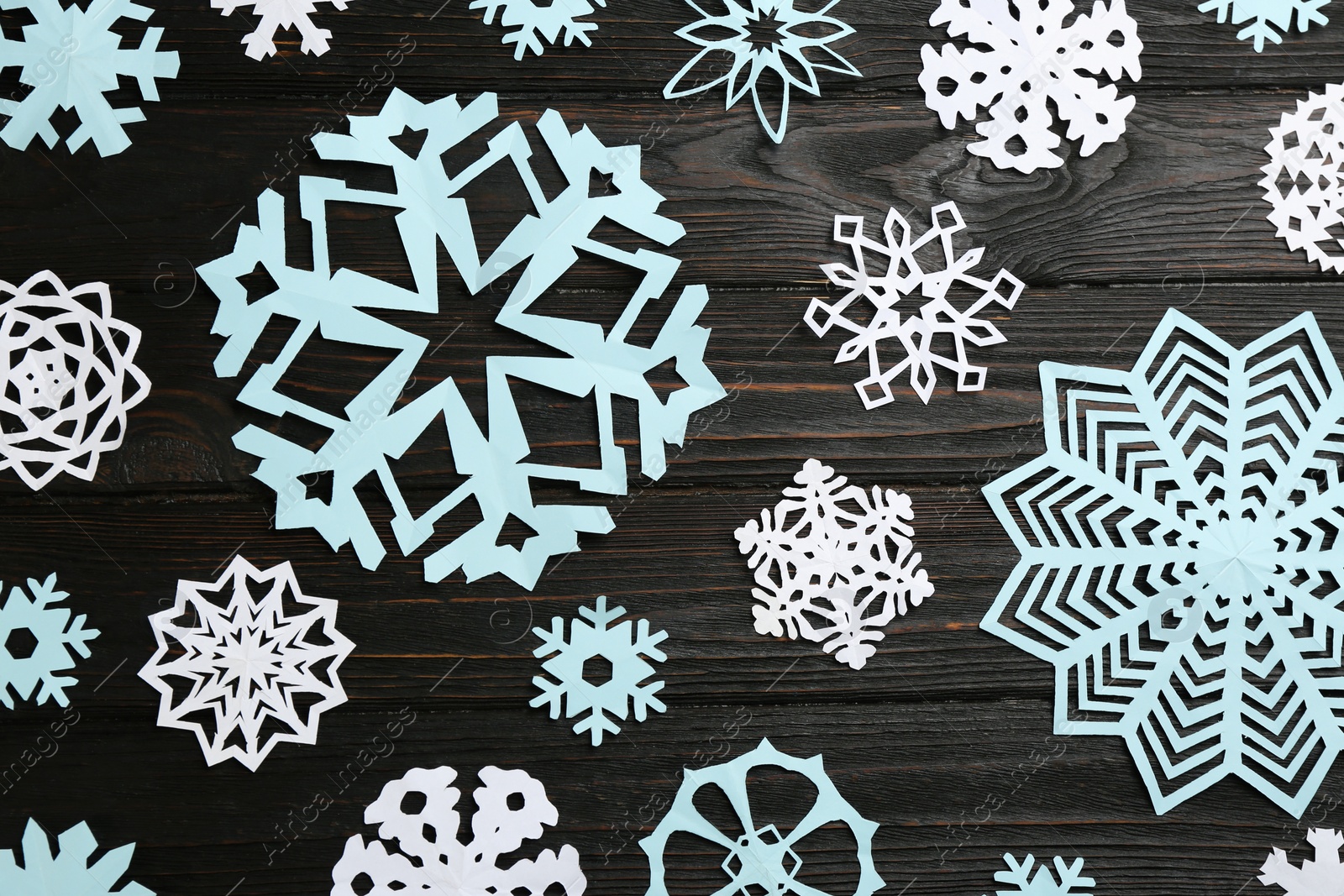 Photo of Different paper snowflakes on black wooden table, flat lay