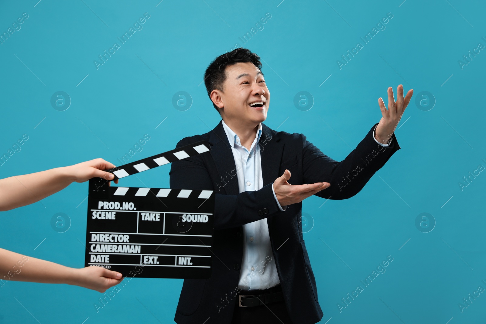 Photo of Happy asian actor performing while second assistant camera holding clapperboard on light blue background. Film industry