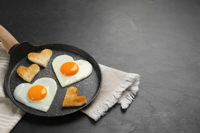 Photo of Heart shaped fried eggs and toasts in frying pan on grey table, space for text