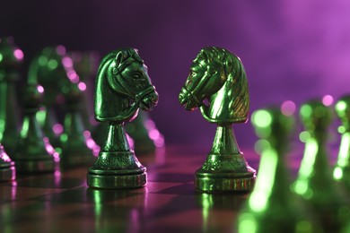 Photo of Two knights and other chess pieces on checkerboard in color light, closeup