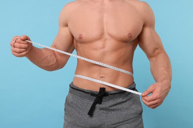 Photo of Athletic man measuring waist with tape on light blue background, closeup. Weight loss concept