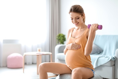 Photo of Young pregnant woman doing exercises with dumbbell at home