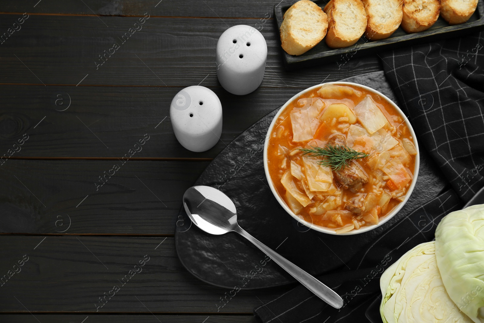 Photo of Tasty cabbage soup with meat, carrot and dill served on black wooden table, flat lay. Space for text